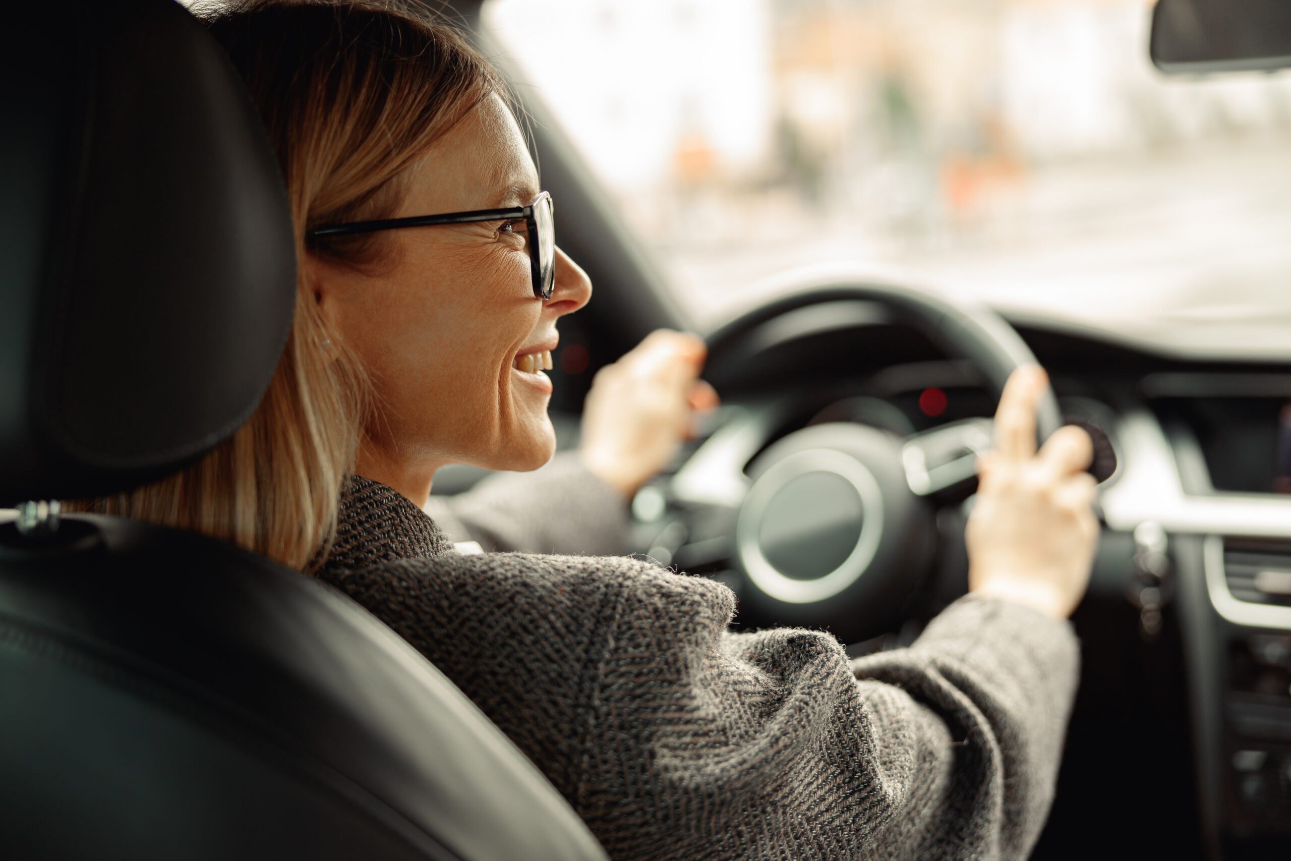 Rear view of smiling woman driving car and holding both hands on steering wheel